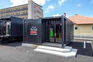 a black shipping container with stairs in a parking lot at HOTEL R9 The Yard Kirishimakokubu in Kirishima