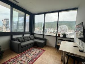 ein Wohnzimmer mit einem Sofa, einem Schreibtisch und Fenstern in der Unterkunft Axis Towers 1 bedroom 4 guests! in Tbilisi City