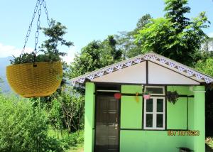 un pequeño edificio verde y blanco con una cesta colgante en Dhim Farmstay, en Namchi