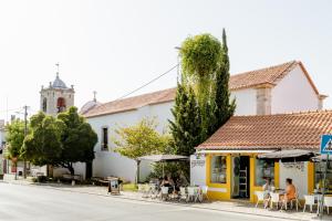 una calle con un edificio amarillo y blanco con gente sentada en las mesas en Arrábida Guest Studio, en Aldeia Rica
