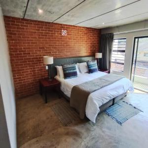 a bedroom with a bed and a brick wall at The Wild Peach - Menlyn in Pretoria