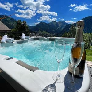 una vasca idromassaggio con una bottiglia e due bicchieri di vino di Chalet Familial Le Whymper 5 étoiles SPA Sauna Chatel a Châtel