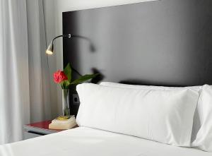 a bed with a white pillow and a red table with a rose at SM Hotel Sant Antoni in Barcelona