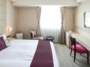 a hotel room with a bed and a desk and chairs at Vessel Inn Shigamoriyamaekimae in Moriyama