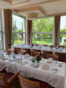 un comedor con mesas y sillas blancas y ventanas en Strandhotel Löchnerhaus en Reichenau