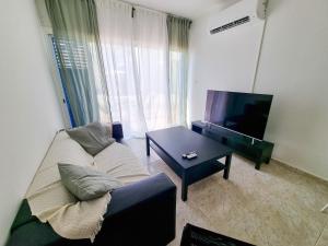 ein Wohnzimmer mit einem Sofa, einem TV und einem Tisch in der Unterkunft Beach Vibes Apartment in Pyla