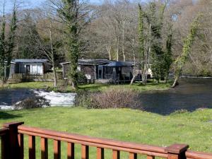 eine Holzbank vor einem Haus neben einem Fluss in der Unterkunft Pass the Keys Comfortable 2 Bed Riverside Chalet near Snowdonia in Caernarfon