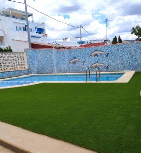 a swimming pool with green grass next to a wall at Anamar Kione Rentals in Alcossebre