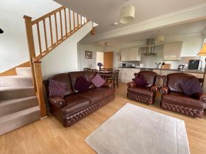 a living room with two leather couches and a kitchen at Blaeberry Cottage in Killean