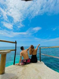 a man and woman sitting on a pier looking at the ocean at Stay N Save B&B in Oslob