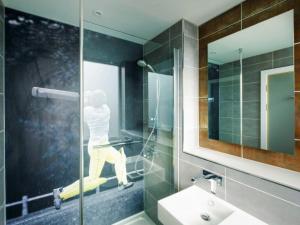 een badkamer met een glazen douche en een persoon op een bed bij ibis Styles Leeds City Centre Arena in Leeds