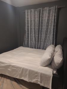a bed with white sheets and pillows in front of a window at West Homestays Kodi2518 in Nairobi