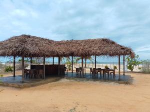a restaurant with tables and chairs under a straw roof at Hotel arugambay beach inn resort in Arugam Bay
