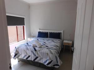 Un dormitorio con una cama con sábanas azules y blancas y una ventana en The Cottage, en Krugersdorp