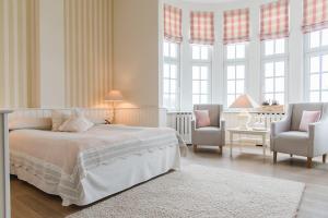 a white bedroom with a bed and two chairs at Strandhotel Glücksburg in Glücksburg