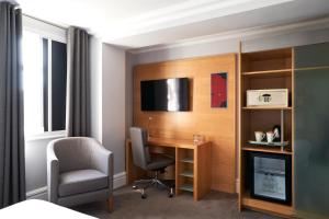 um quarto com uma secretária, uma cadeira e uma televisão em Thistle London Park Lane em Londres