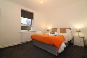 a bedroom with a bed with an orange blanket and a window at Signature - Carrick View in Cumbernauld
