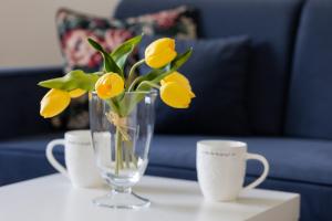 a vase with yellow flowers on a table with cups at Comfy Apartment Powstańców Śląskich by Renters in Warsaw