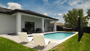 a pool with two chairs and a hammock next to a house at Corallo House - Heated Pool in Cape Coral