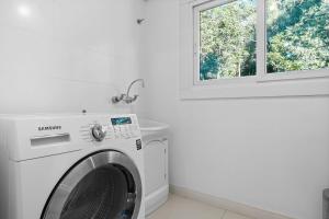 uma máquina de lavar roupa numa lavandaria branca com uma janela em Residencial Villa Verde - 403 B em Gramado