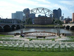 a group of chairs sitting in the grass near a river at Embassy Suites Des Moines Downtown in Des Moines