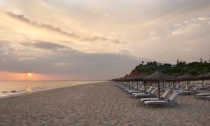 a row of beach chairs and umbrellas on a beach at Conrad Algarve in Quinta do Lago