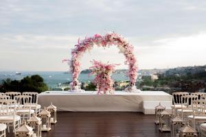 イスタンブールにあるコンラッド イスタンブール ボスポラスの花のアーチと白い椅子が備わるウェディングテーブル