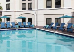 a swimming pool with blue chairs and umbrellas at Hampton Inn & Suites Miami-Doral Dolphin Mall in Miami