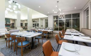 Hilton Garden Inn Oakland/San Leandro في سان لياندرو: مطعم بطاولات بيضاء وكراسي ونوافذ