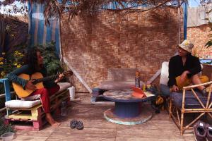 dos personas sentadas en sillas tocando guitarras en un patio trasero en Hostel Posada de Gallo, en Arica