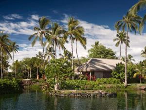 ein Haus mit Palmen vor einem Wasserkörper in der Unterkunft Kona Village A Rosewood Resort in Kailua-Kona