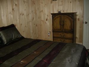 een slaapkamer met een bed en een houten kast bij Chalet des Noisetiers in Tadoussac