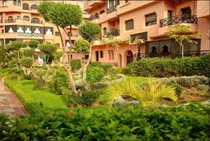 un jardin en face d'un grand bâtiment dans l'établissement APPARTEMENT COSY Au PALMERAIE VILLAGE - 5 PISCINES, à Marrakech