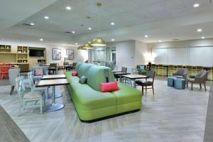 Home2 Suites By Hilton Duncan في دنكان: مكتبة بها أريكة خضراء وطاولات وكراسي