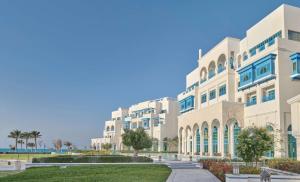 een groot wit gebouw met bomen ervoor bij Hilton Salwa Beach Resort and Villas 