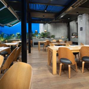 a restaurant with wooden tables and chairs and a cafeteria at Salvio Parque 93 Bogota, Curio Collection by Hilton in Bogotá