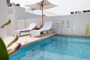 una piscina con 2 sillas blancas y una sombrilla en Nacar Hotel Cartagena, Curio Collection by Hilton, en Cartagena de Indias