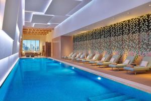 DoubleTree by Hilton Sharjah Waterfront Hotel And Residences في الشارقة: مسبح في فندق مع كراسي صالة ومسبح