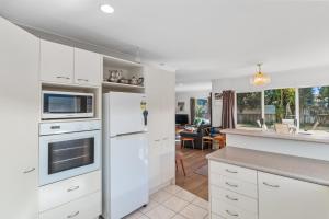 a kitchen with white appliances and a living room at Fisherman's Friend - Bowentown Holiday Home in Waihi