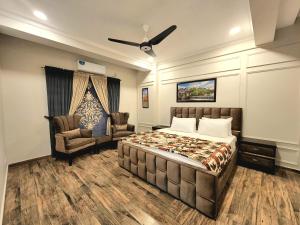 a bedroom with a bed and two chairs and a ceiling fan at The Chromatic Apartments Bahria Town in Rawalpindi +22 photos