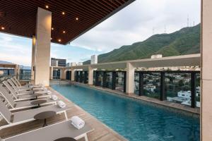 uma piscina do hotel com espreguiçadeiras e montanhas ao fundo em Hilton Monterrey em Monterrey