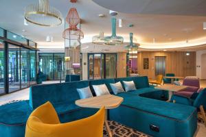 Hampton By Hilton Bialystok في بياويستوك: غرفة معيشة مع أريكة زرقاء وطاولات وكراسي