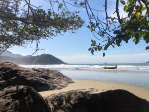 a beach with a boat in the water and rocks at Apartamento Peruíbe com vista para o mar in Peruíbe