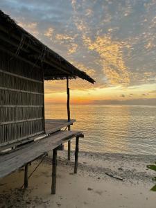 a hut on the beach with a sunset in the background at West Mansuar Homestay in Pulau Mansuar