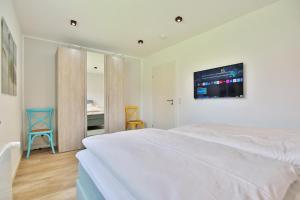 a bedroom with a white bed with a tv on the wall at Haus am Seehof 9 Ferienwohnung Ostseeliebe Nr 3 in Sierksdorf