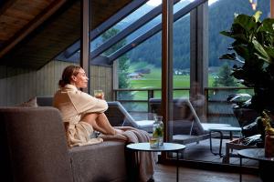 a woman sitting on a couch with a glass of wine at Hotel Quelle Nature Spa Resort in Santa Maddalena in Casies