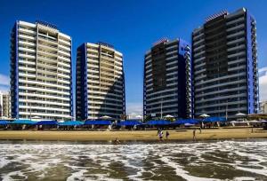 tres edificios altos con sombrillas azules en una playa en Lujoso Condominio Frente al Mar en Tonsupa, Ecuador, en Tonsupa