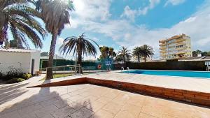 a swimming pool with palm trees and a building at GENIETEN OP HET STRAND in Miami Platja
