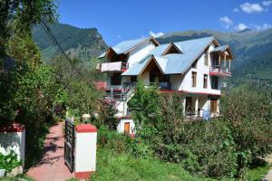 a large white house on a hill with mountains in the background at The Cozy Nook - Manali in Manāli