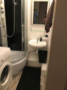 a bathroom with a sink and a shower and a washing machine at Przytulny apartament z bezpłatnym parkingiem in Olsztyn